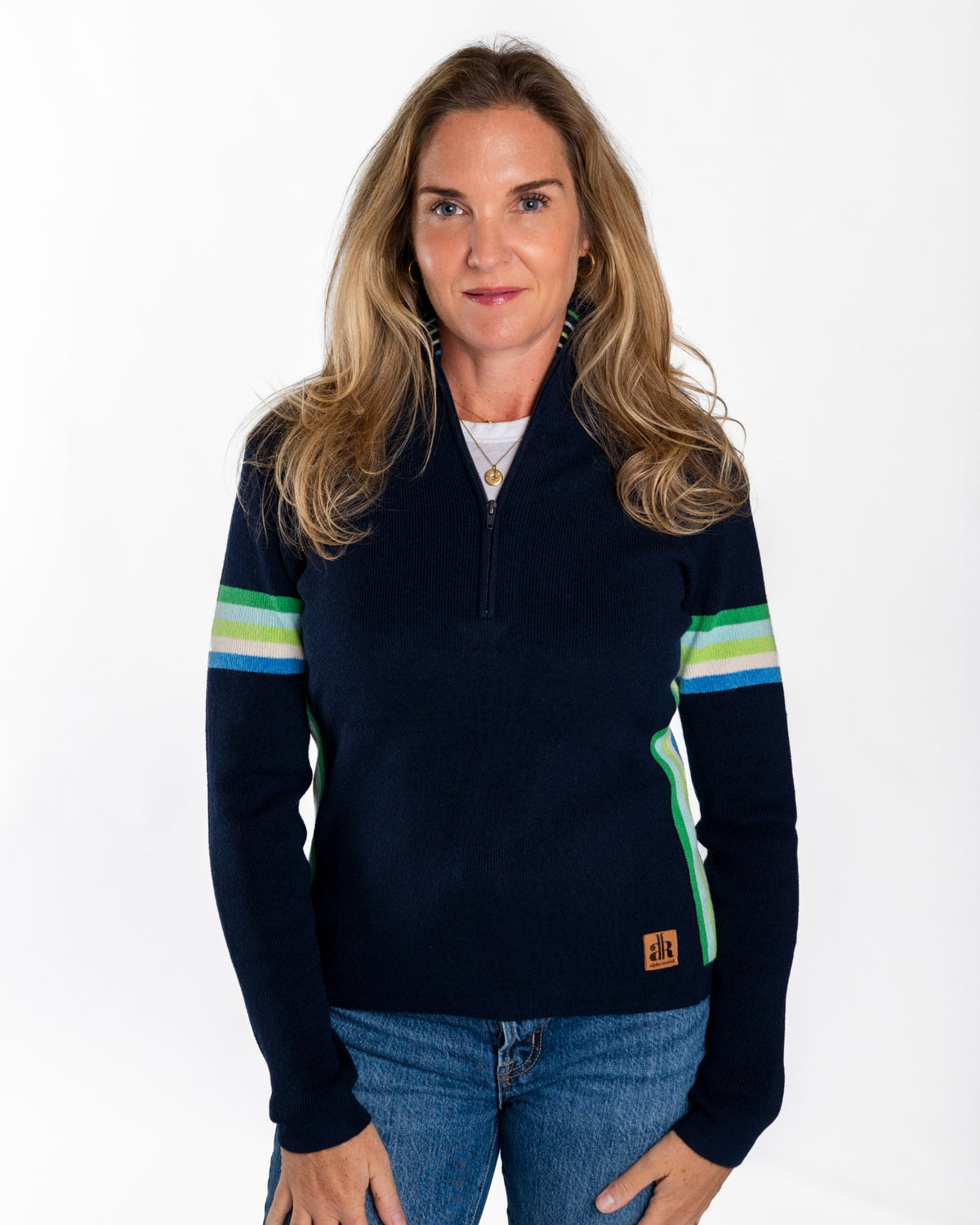 A woman modeling a navy blue quarter-zip sweater with green and light blue stripes on the sleeves, paired with blue jeans, against a plain white background. - Navy