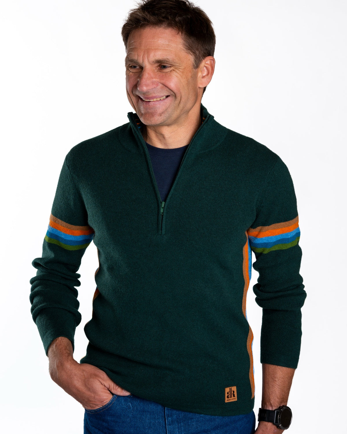 A smiling man wearing a dark green quarter-zip sweater with orange and blue striped accents on the sleeves, paired with blue jeans, against a plain white background. - British Race Green