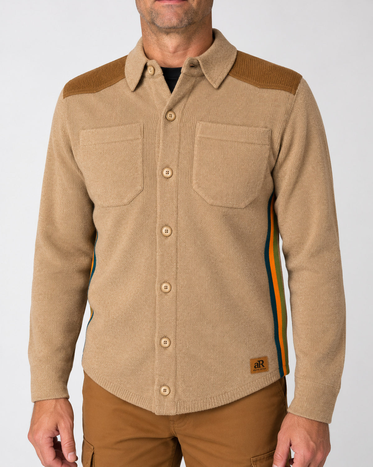 A man wearing a beige knit button-up shirt-jacket with brown ribbed shoulder yoke panels, two chest pockets, and thin multicolor side stripes in blue, orange, and green. The jacket has a small brown patch on the lower hem with the brand name 'BXR'. - Clay
