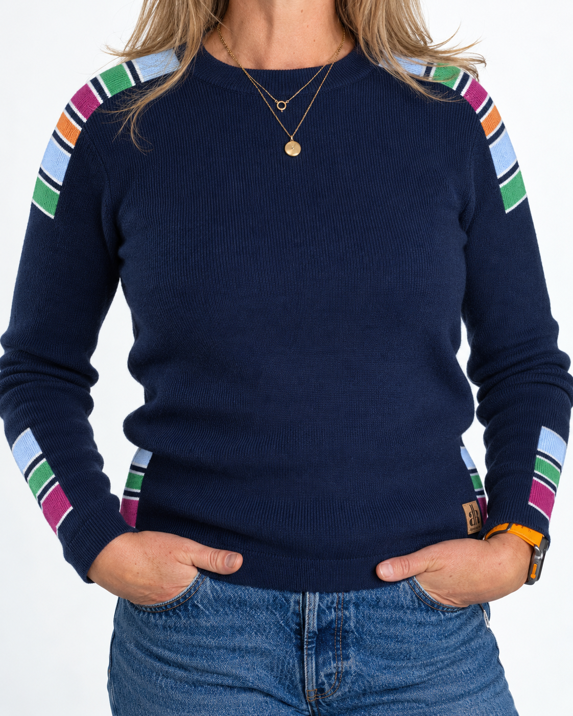 A woman wearing a navy blue crewneck sweater with colorful striped shoulder and sleeve panels, paired with blue jeans and layered gold necklaces. - Navy