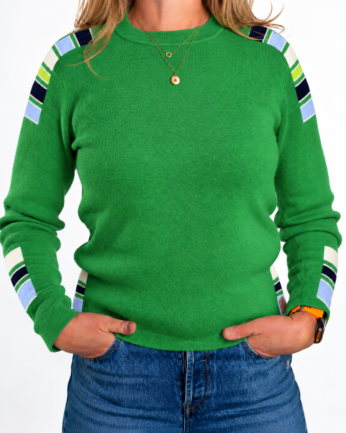 A woman wearing a bright green crewneck sweater with striped shoulder and sleeve accents in navy, lime green, light blue, and white, paired with blue jeans. - Kelly Green