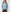 A woman wearing a light blue knit pullover hoodie with white drawstrings and subtle side stripe accents, paired with dark jeans, against a plain light gray studio background. - Sea
