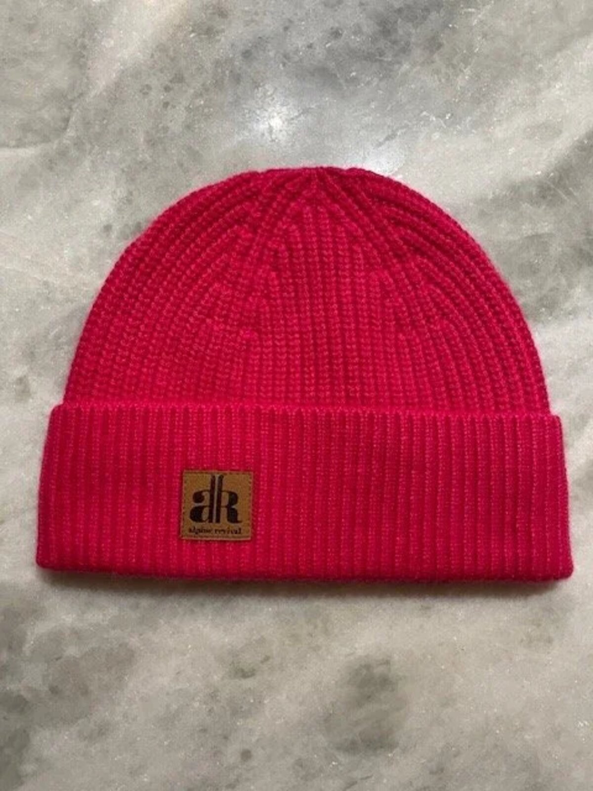 Red knit beanie with a brand logo on a gray surface