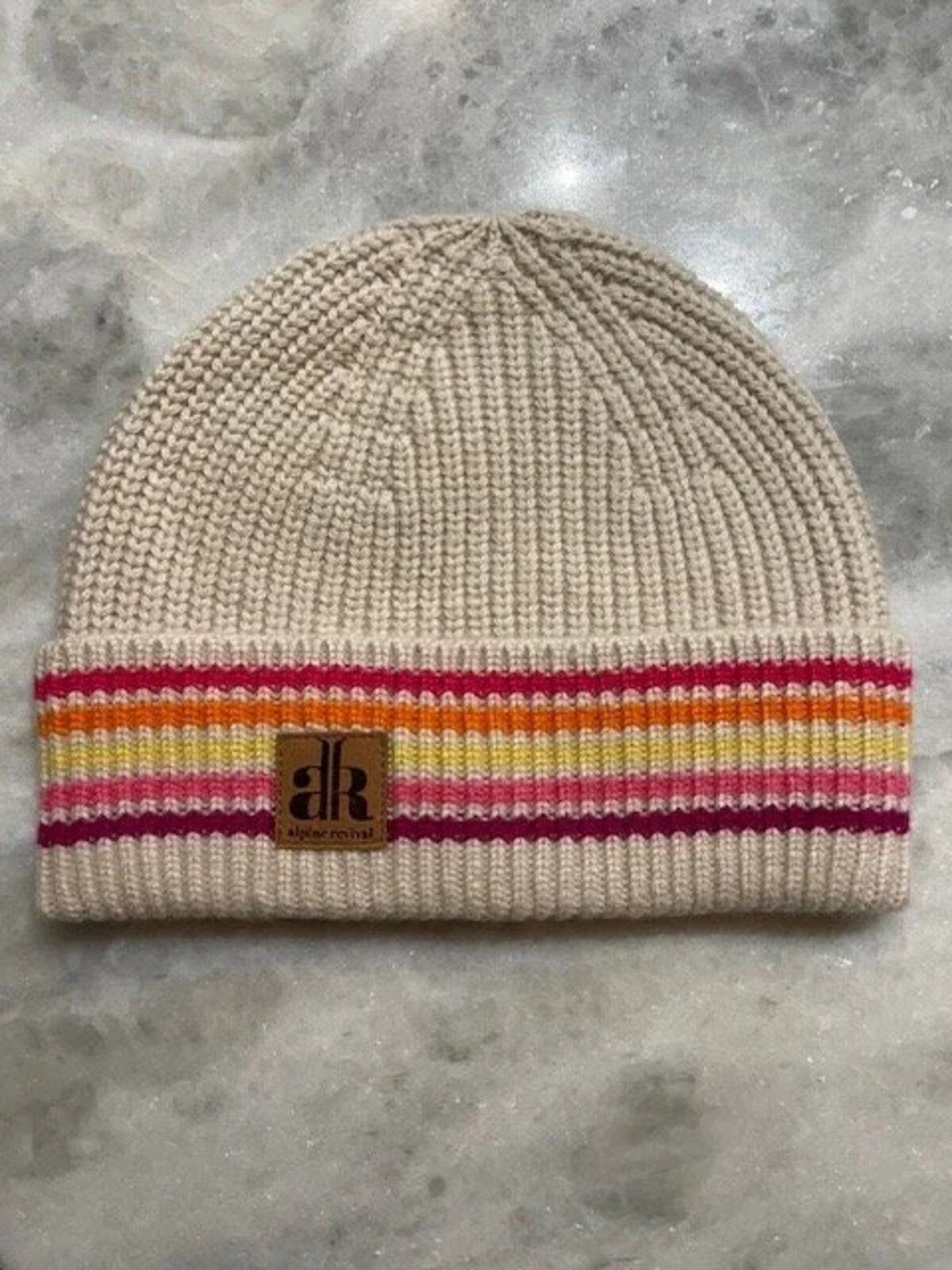 Beige knit beanie with colorful stripe and brand logo on a gray surface
