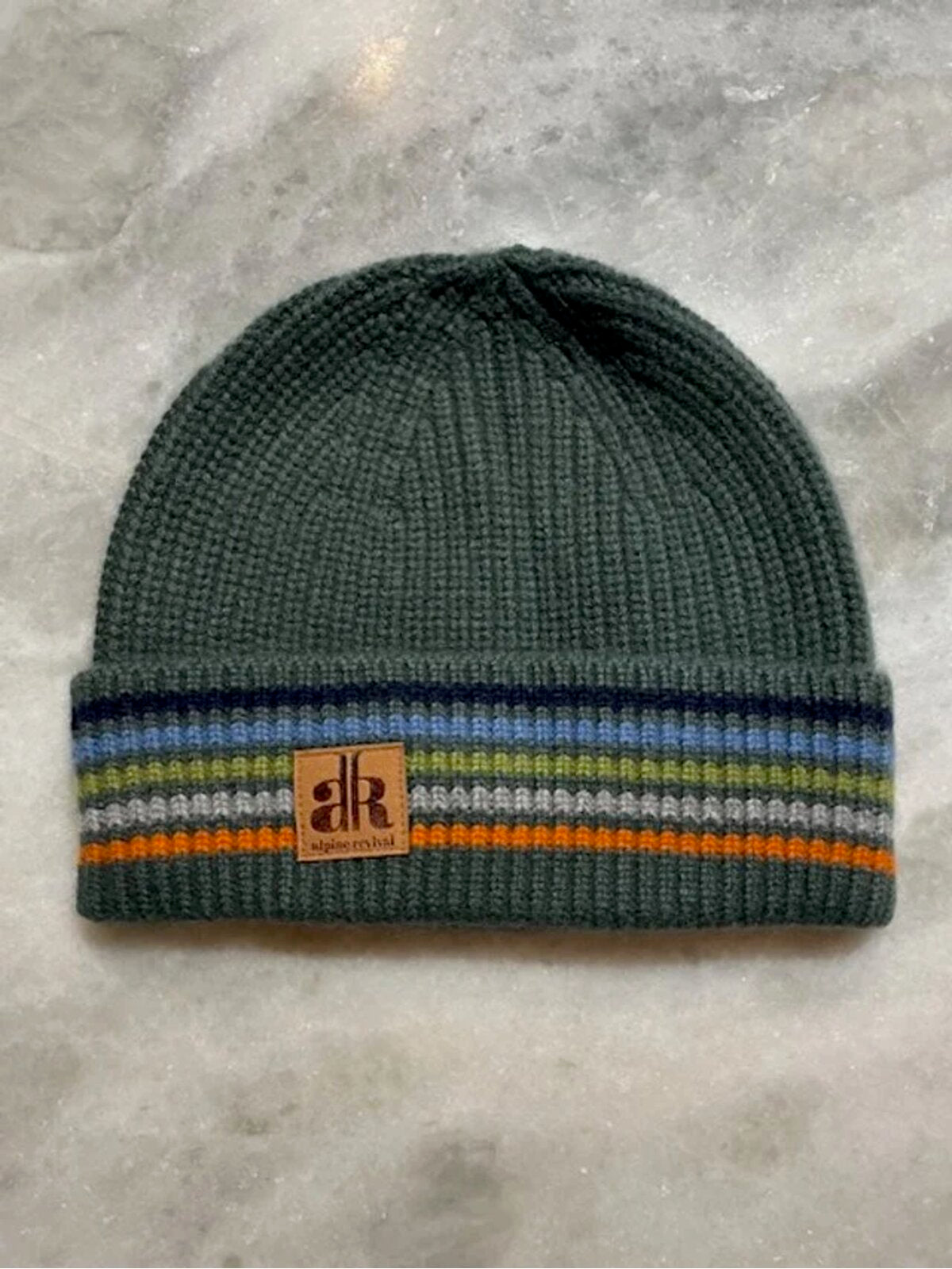 Green beanie with striped pattern and brand logo on a gray surface