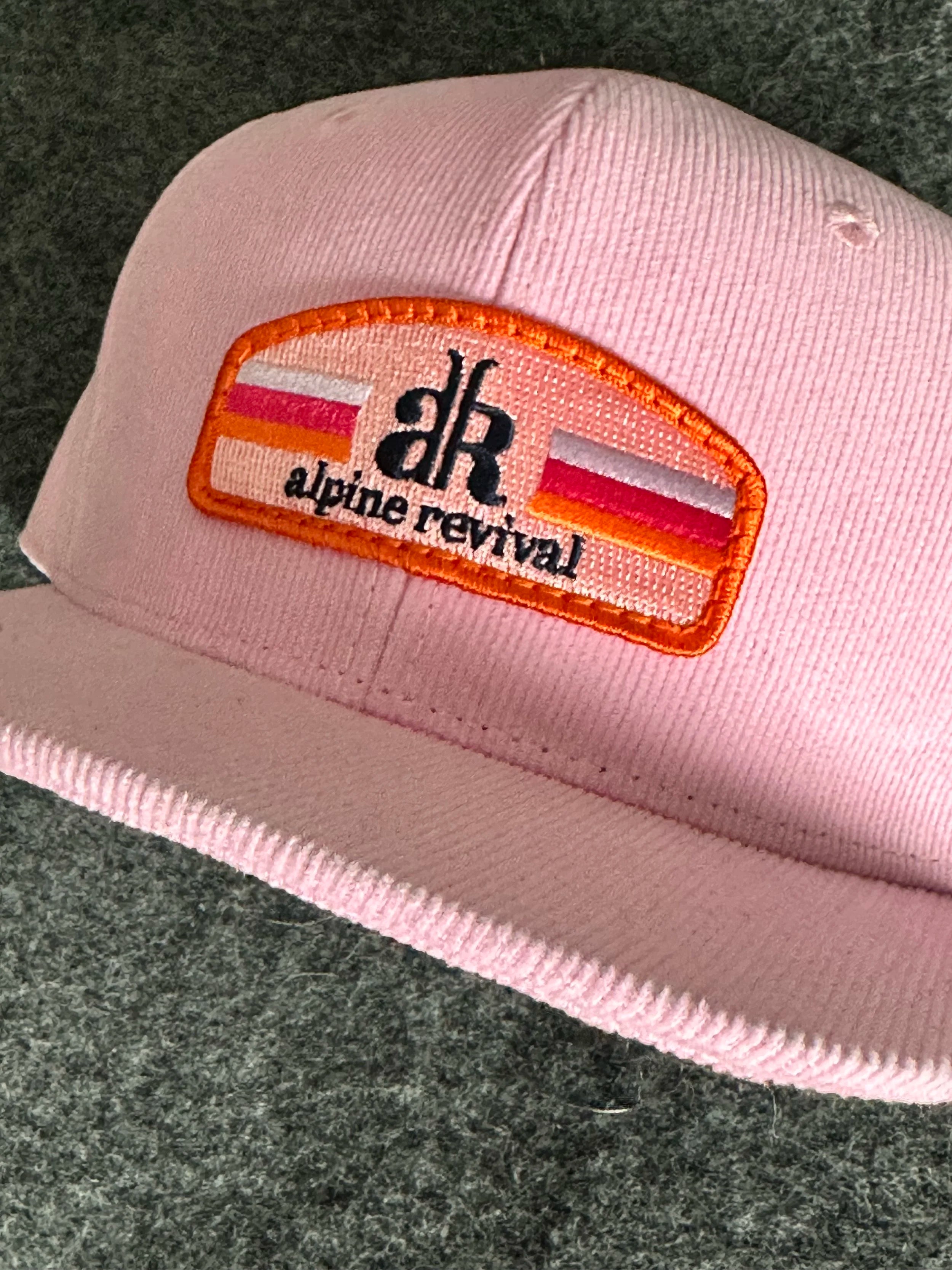 Pink cap with a patch featuring 'alpine revival' logo on a dark textured background
