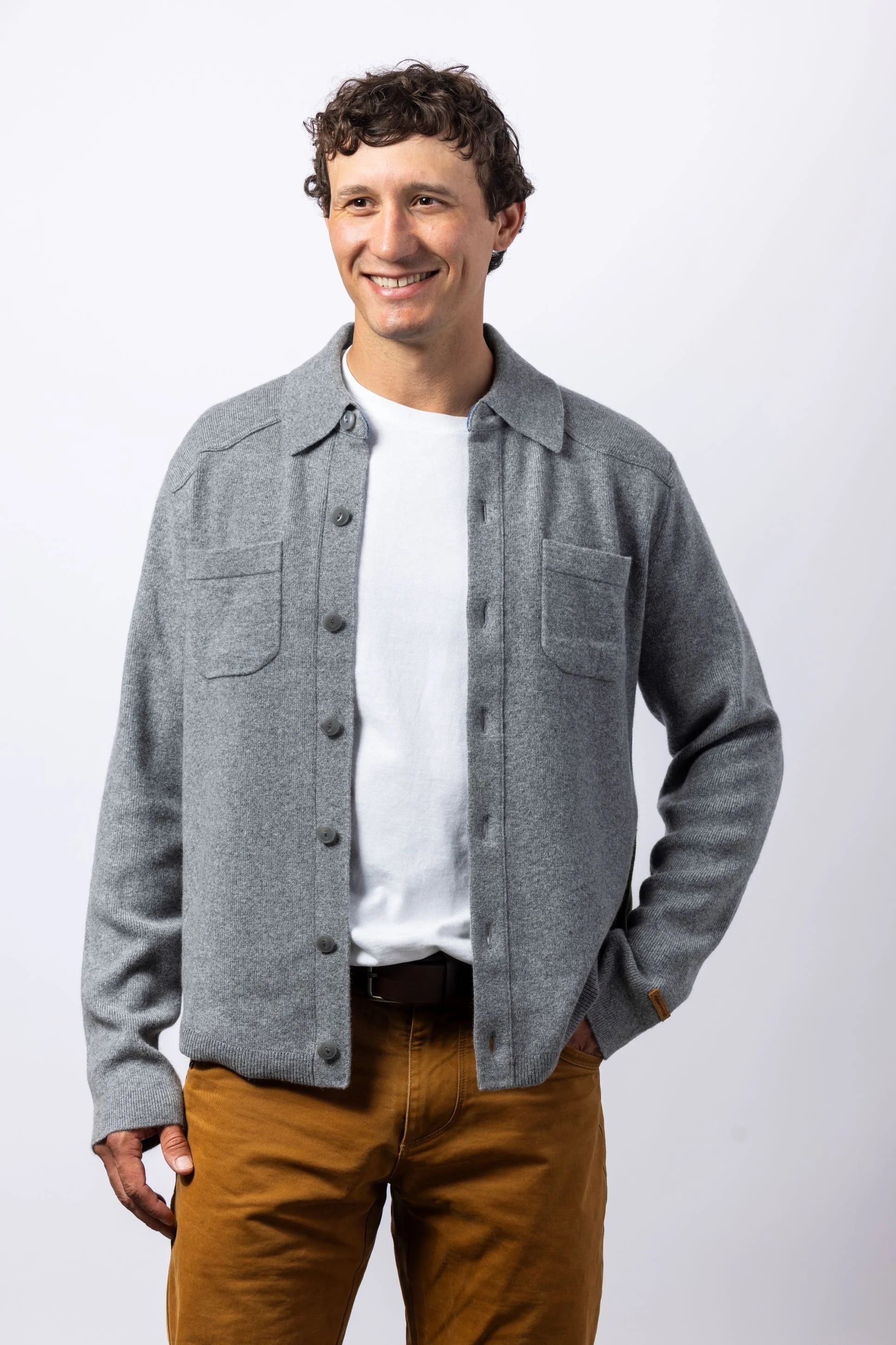 Man wearing a gray jacket over a white shirt and brown pants on a white background