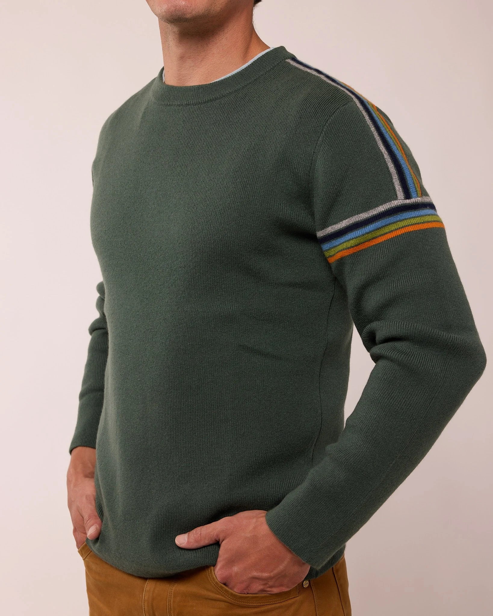 Green sweater with striped sleeves worn by a person on a plain background