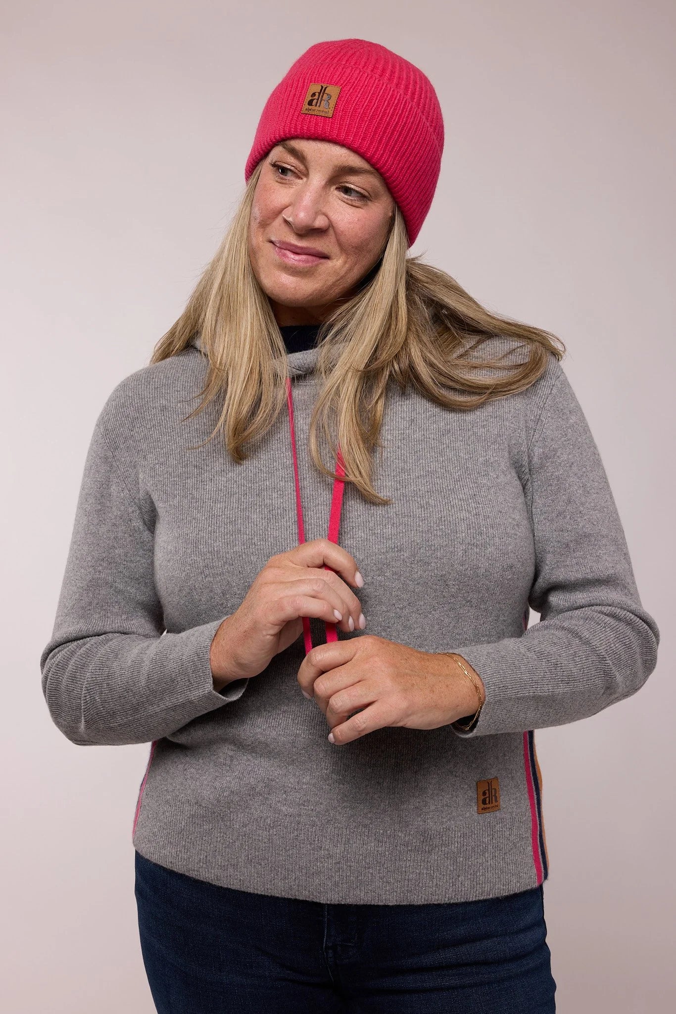 Woman wearing a gray sweater with pink accents and a red beanie on a plain background