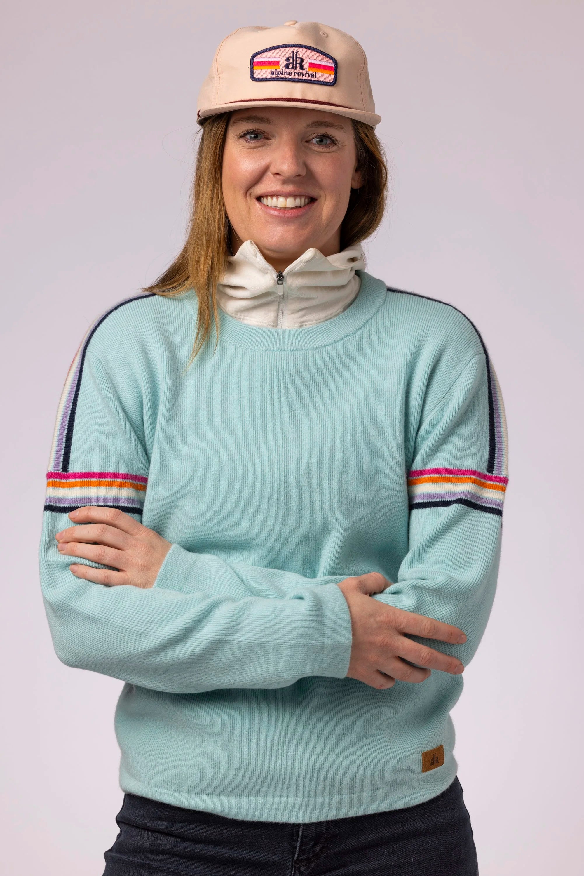 Person wearing a light blue sweater with arm stripes and a beige cap on a white background