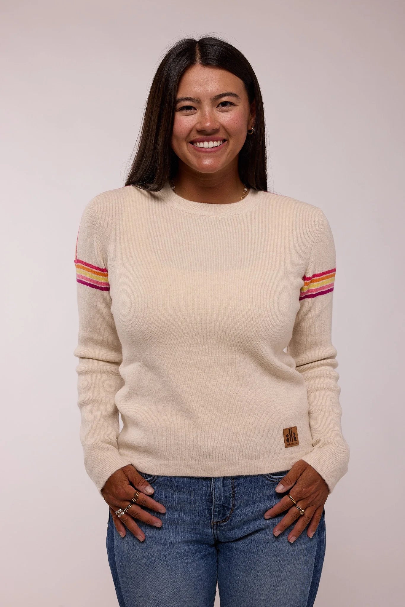Woman wearing a beige sweater with colorful stripes on a plain background