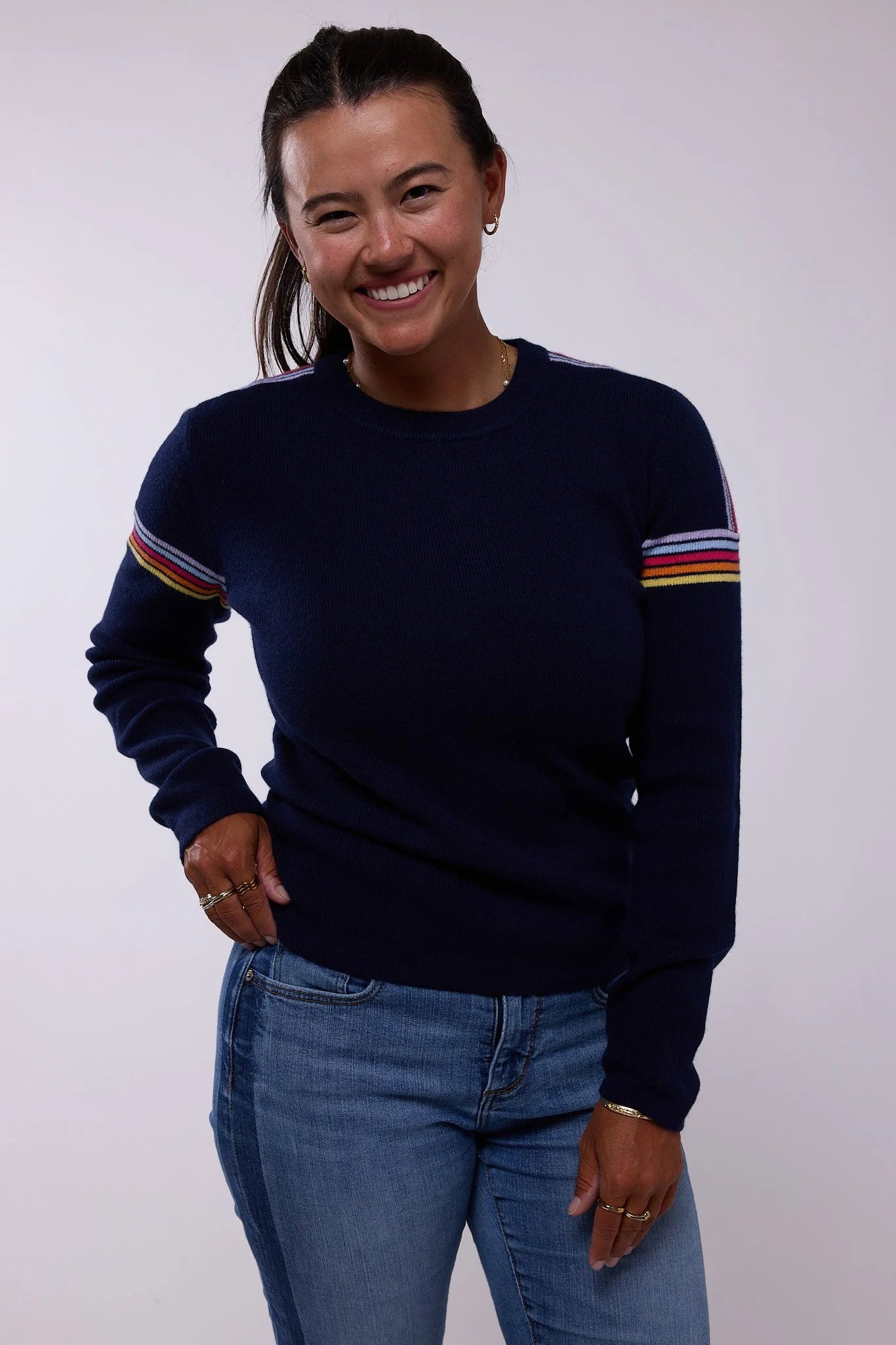 Woman wearing a navy sweater with colorful stripes on a white background