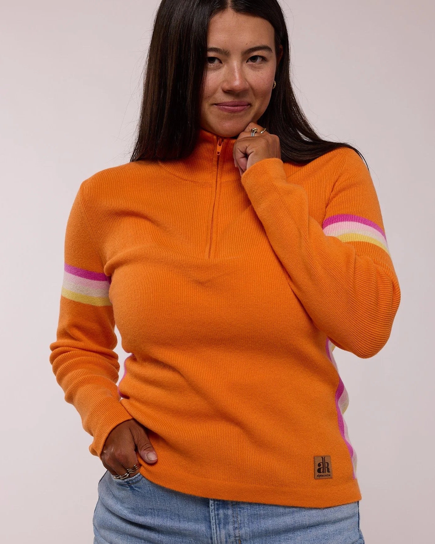 Woman wearing an orange sweater with colorful stripes on a plain  background - Sunset