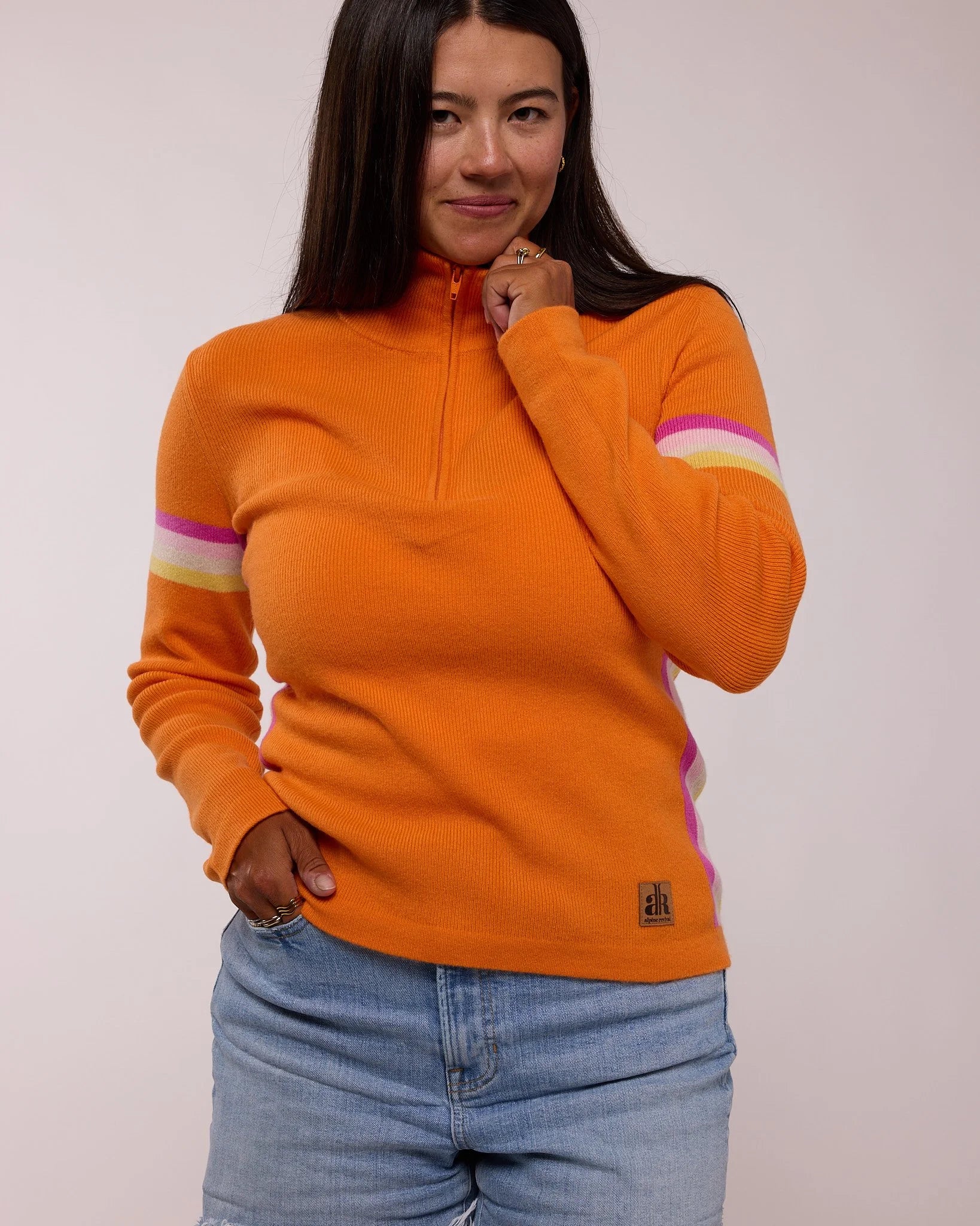 Woman wearing an orange sweater with colorful stripes on a plain background